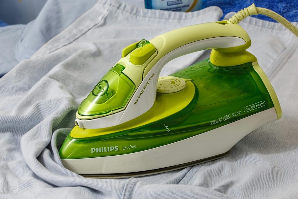 Green Philips EcoCare iron on a wrinkled shirt, ready for ironing.